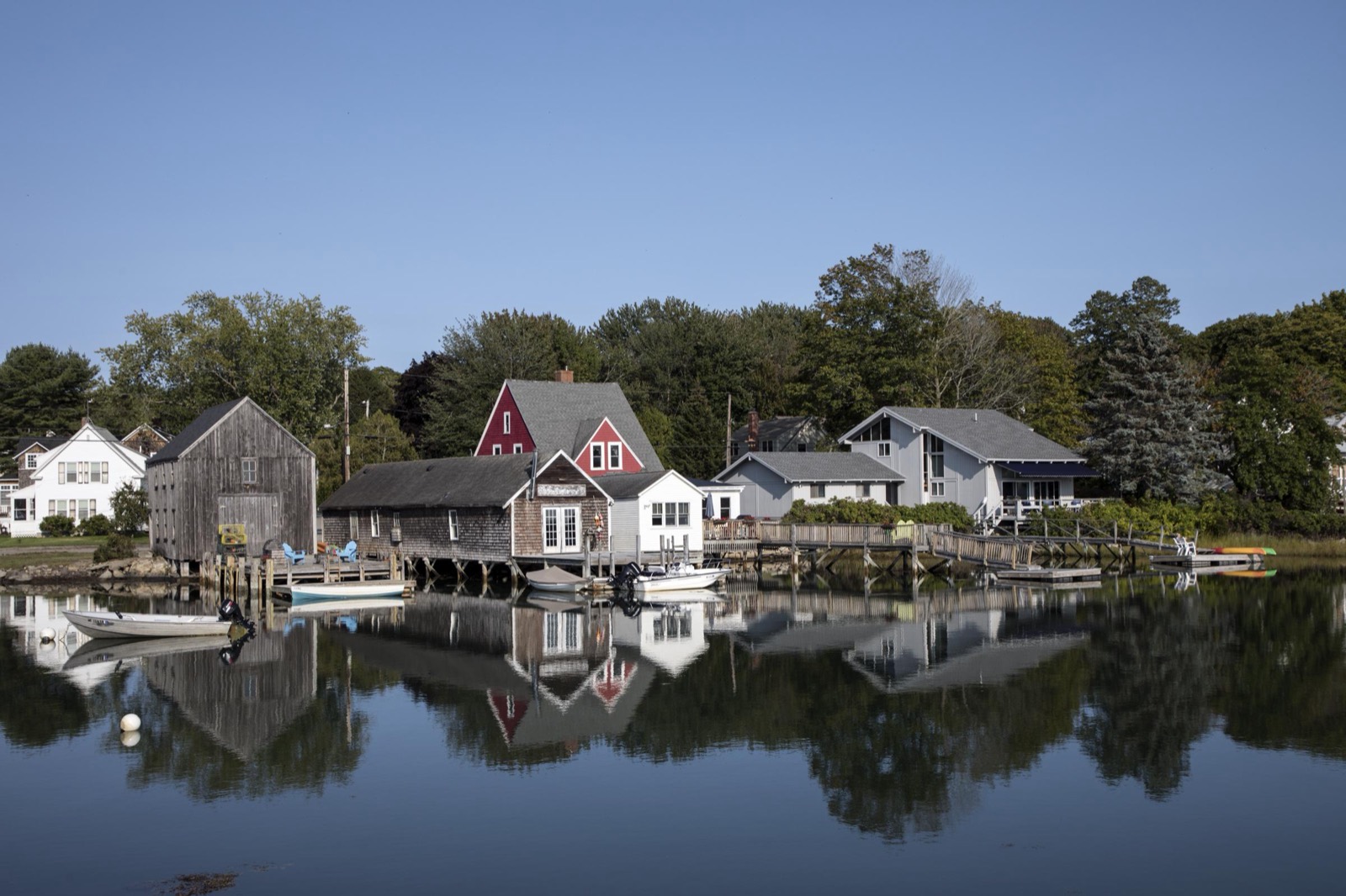Weathered shingled boathouses and cottages reflect in the still water of the harbor at Cape Porpoise, Maine.