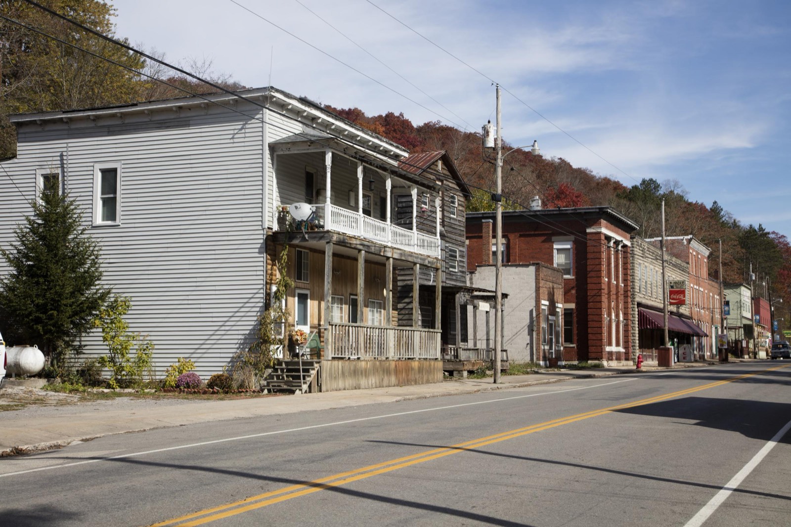 Wood-frame houses with porches and old brick storefronts line the main road through Durbin, West Virginia, with autumn-colored hills behind.