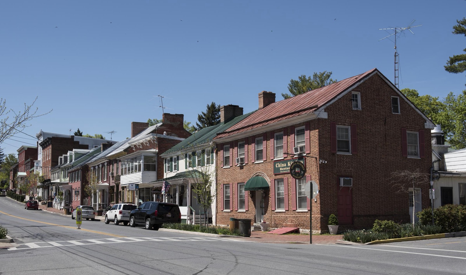 Historic brick and clapboard buildings with colorful shutters line a quiet street in Shepherdstown, West Virginia, on a bright spring day.